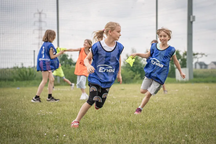 Dzieci biegające po boisku w koszulach z logo Enea