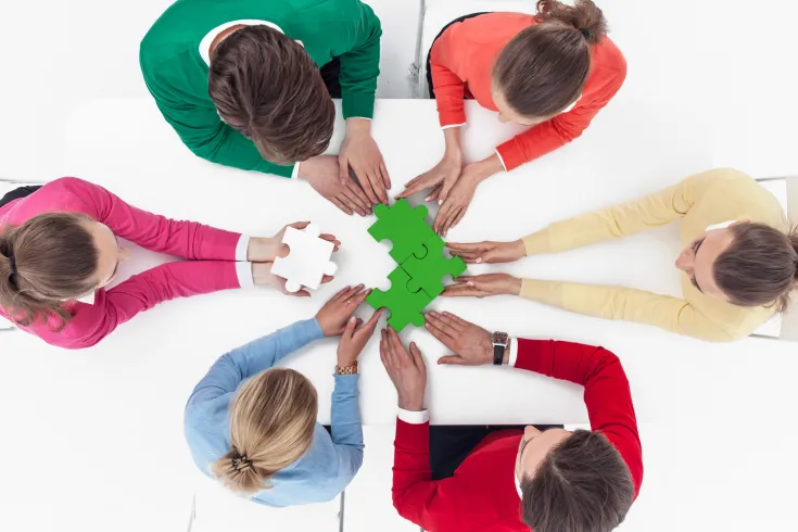 group-people-assembling-jigsaw-puzzle-sitting-around-white-table